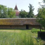 Kirche hinter jungsteinzeitlichem Haus